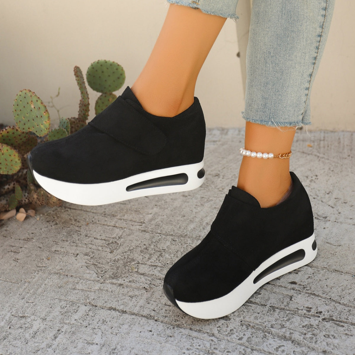 Black slip-on platform sneakers with thick white soles worn with jeans