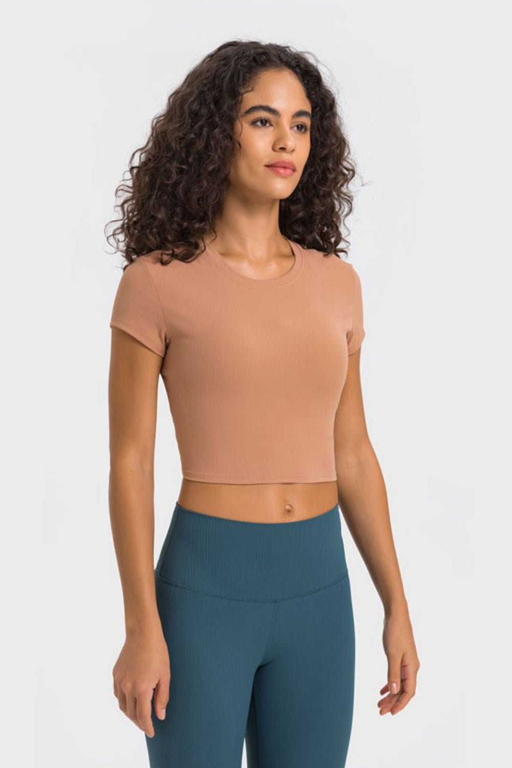Model in peach cropped T-shirt and teal leggings, three-quarter view