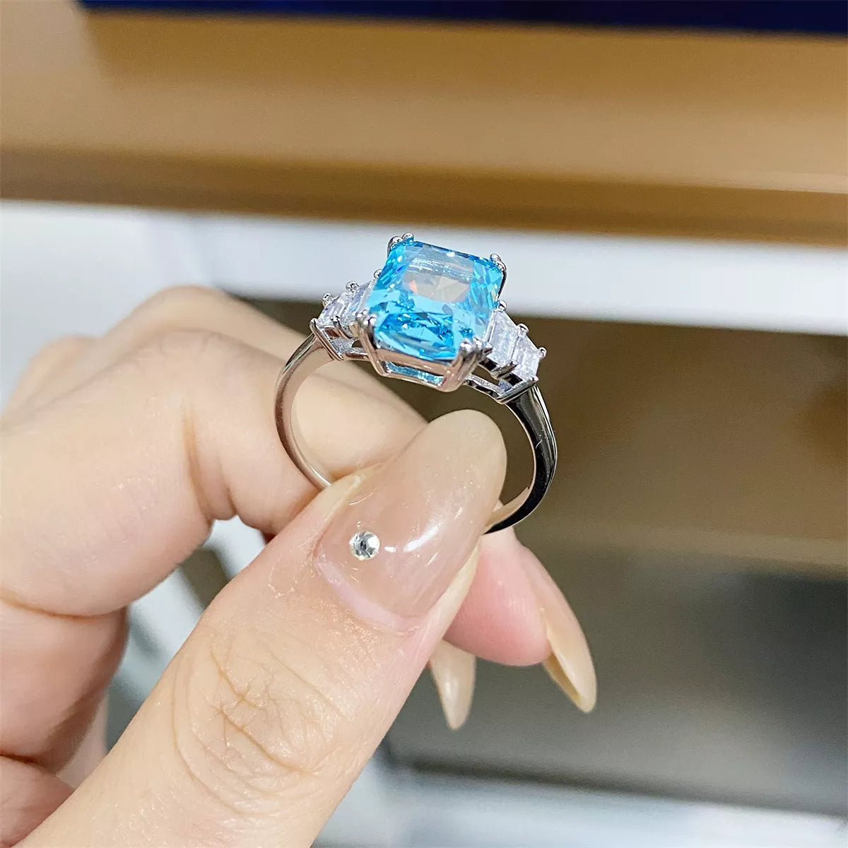Side view of a pastel blue rectangular zircon ring held between fingers