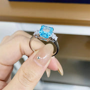Side view of a pastel blue rectangular zircon ring held between fingers