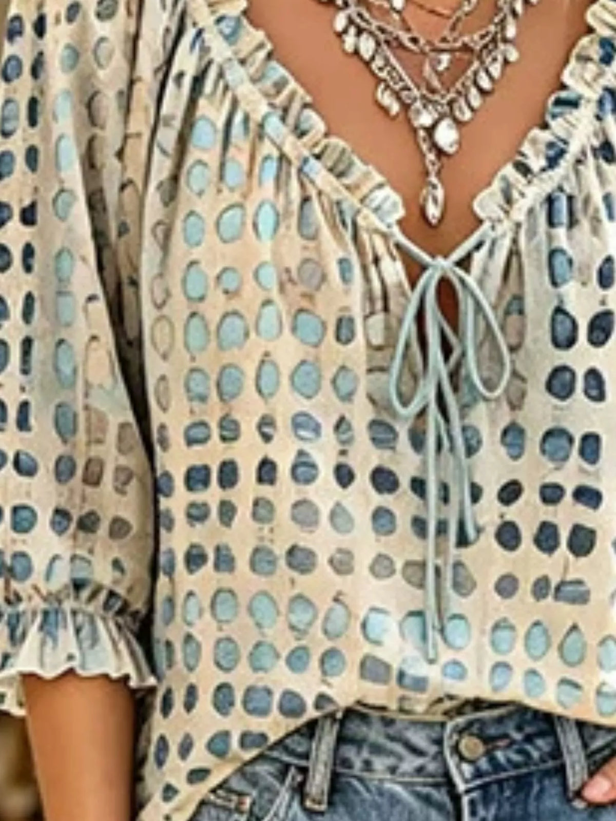 Close-up of beige blouse showing blue and charcoal spots, ruffled neckline and front tie