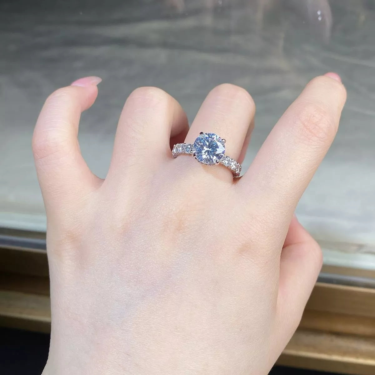 Front view of a bright round-stone ring with a pavé-style band on a hand.