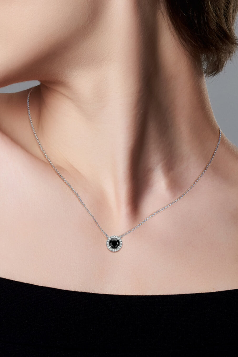 Model wearing a small round black-stone pendant necklace with a black top