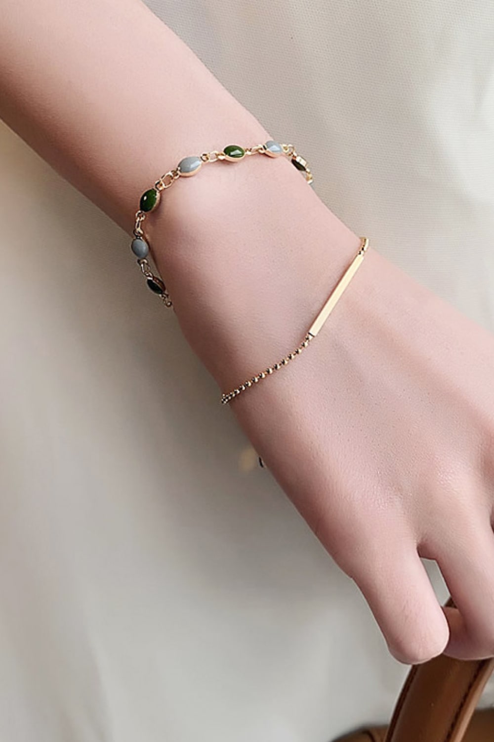 Double-layer gold-tone bracelet with green and pale blue stones and bar detail worn on a wrist