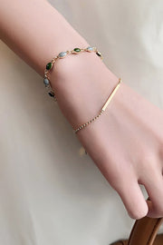 Double-layer gold-tone bracelet with green and pale blue stones and bar detail worn on a wrist