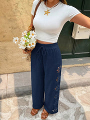 Model in navy embroidered wide-leg pants carrying a woven bag