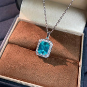 Turquoise-blue rectangular pendant with clear stone halo and silver-tone chain in jewellery box