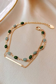 Double-layer gold-tone bracelet with green and pale blue oval stones arranged on a light surface