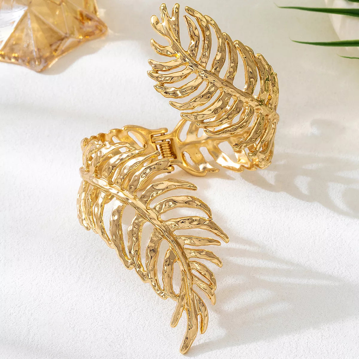 Gold-tone leaf cuff bracelet displayed upright on white surface