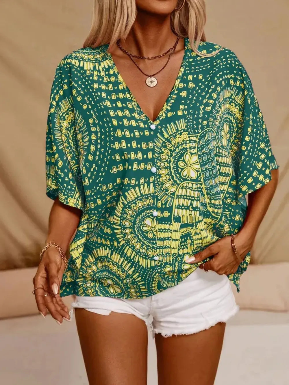 Green medallion-print blouse with tassel ties on a model with hands in white shorts pockets.