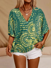 Green medallion-print blouse with tassel ties on a model with hands in white shorts pockets.