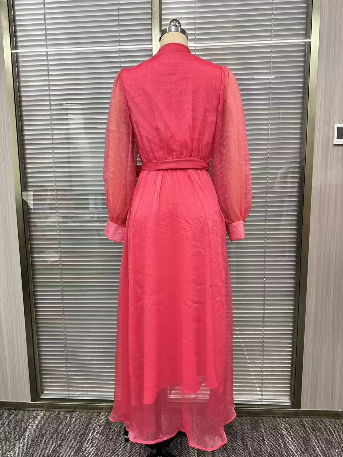 Back view of the pink long-sleeve maxi dress on a dress form, showing its waist tie.