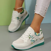 White sneaker with green floral accents and turquoise sole worn at an angle