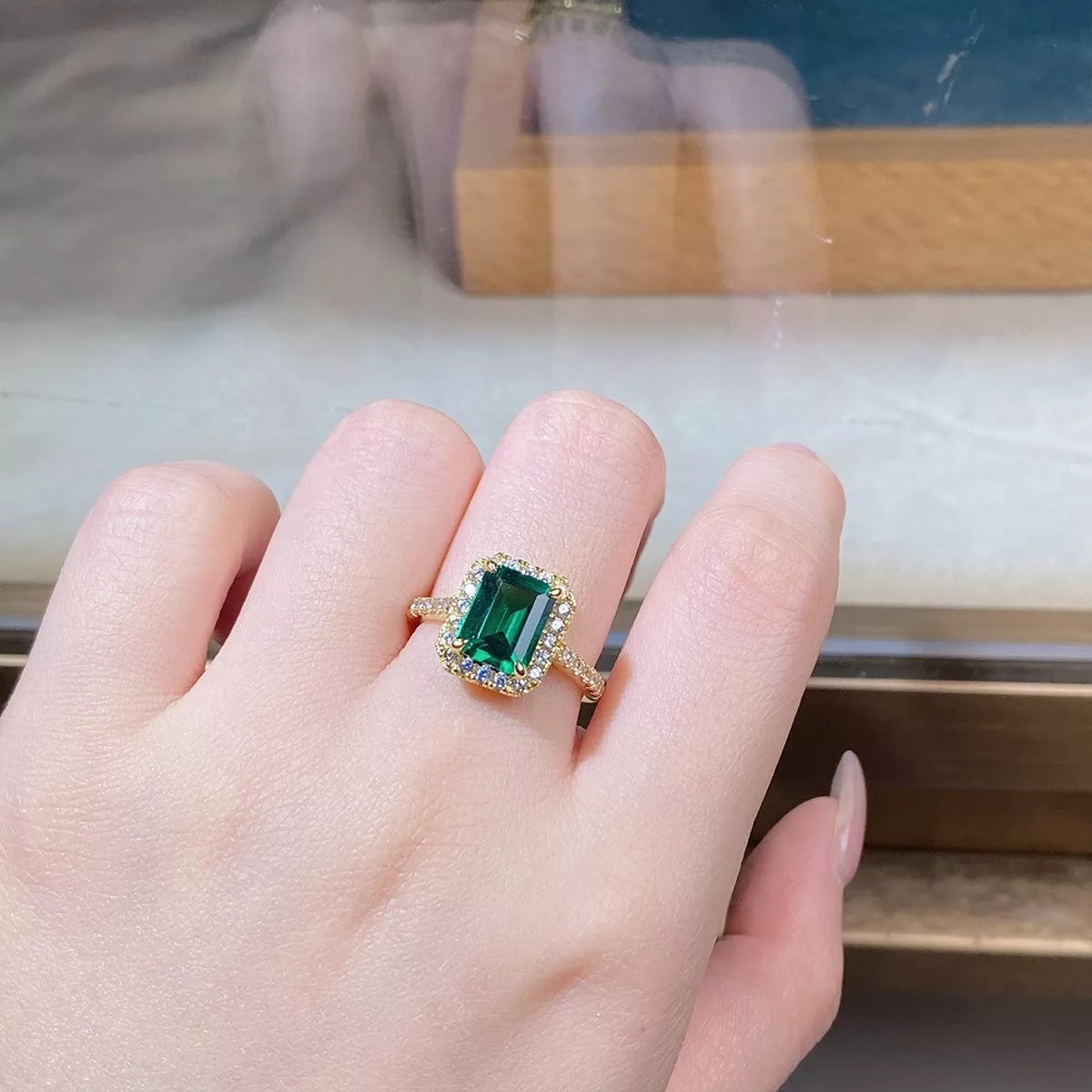Close-up of a green rectangular center stone framed by clear stones on a gold-tone ring.