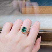 Close-up of a green rectangular center stone framed by clear stones on a gold-tone ring.