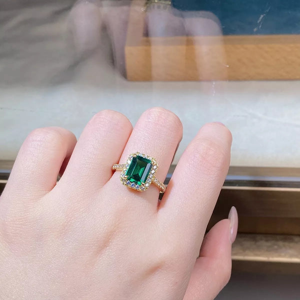Close-up of a green rectangular center stone framed by clear stones on a gold-tone ring.