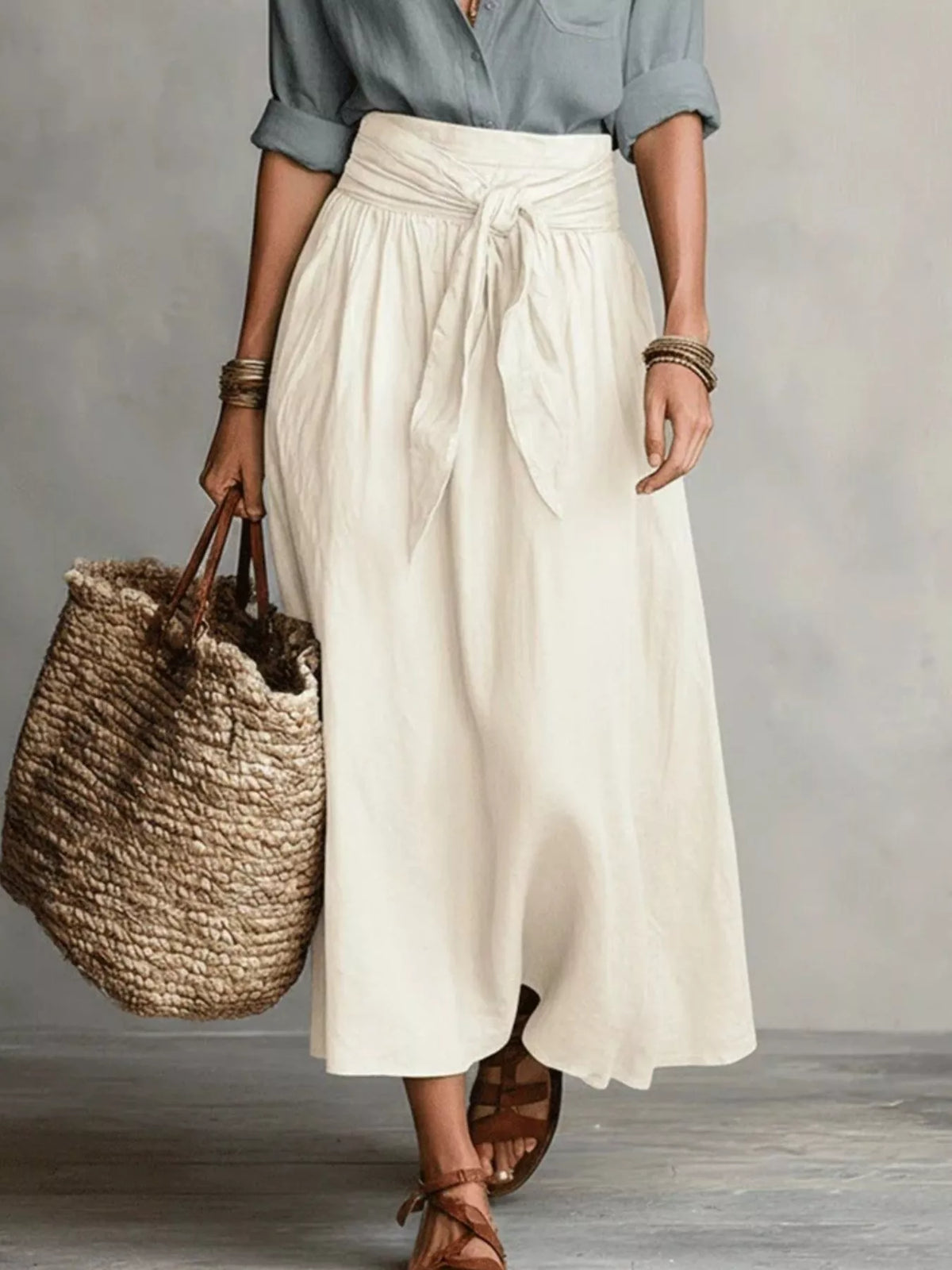 Full-length view of cream midi skirt with a gray button-down shirt and woven tote.