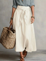 Full-length view of cream midi skirt with a gray button-down shirt and woven tote.