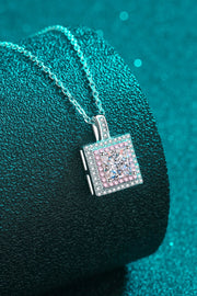 Square pink-bordered pendant necklace draped over a teal cushion