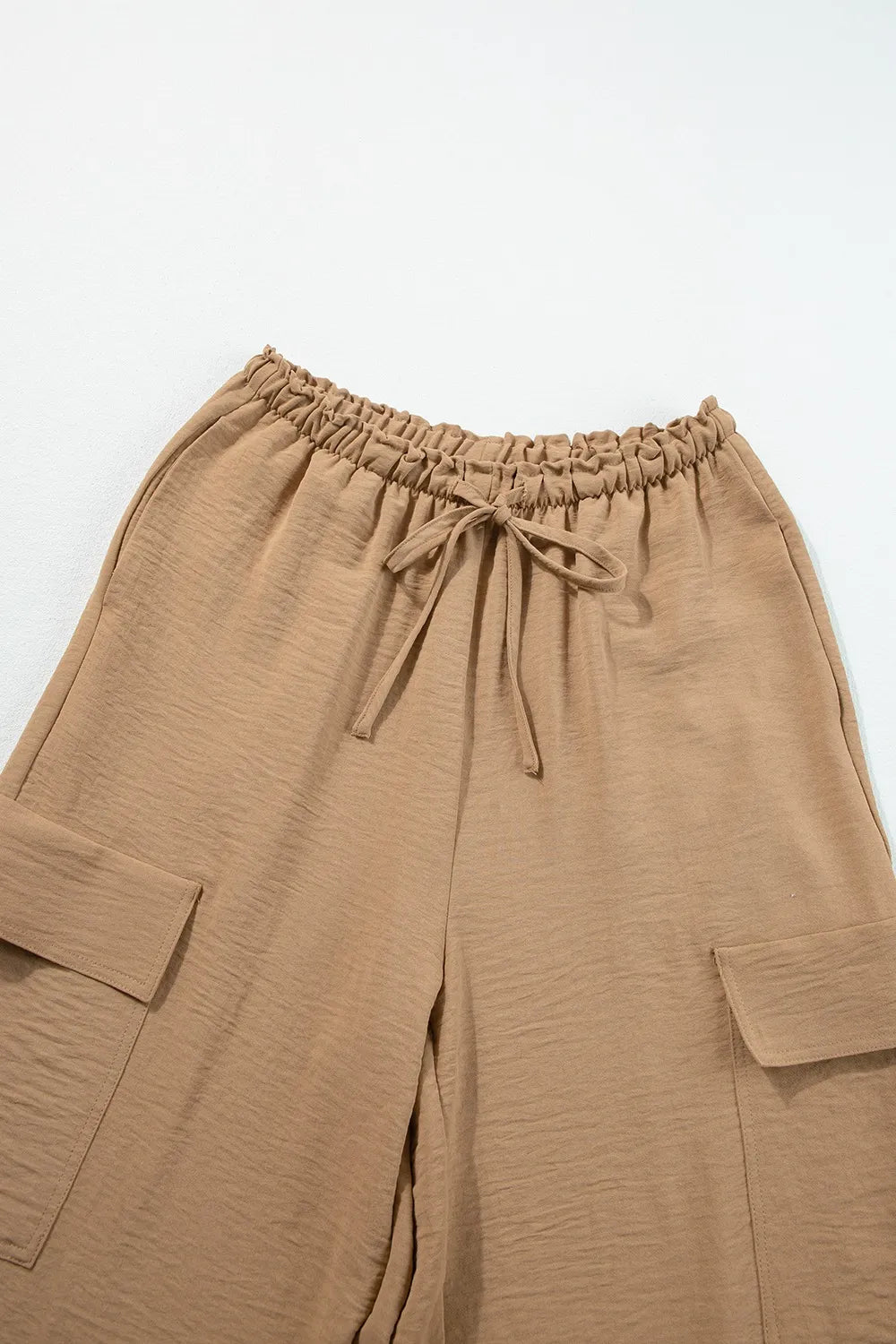 Close view of tan trousers showing the gathered drawstring waist and cargo pockets