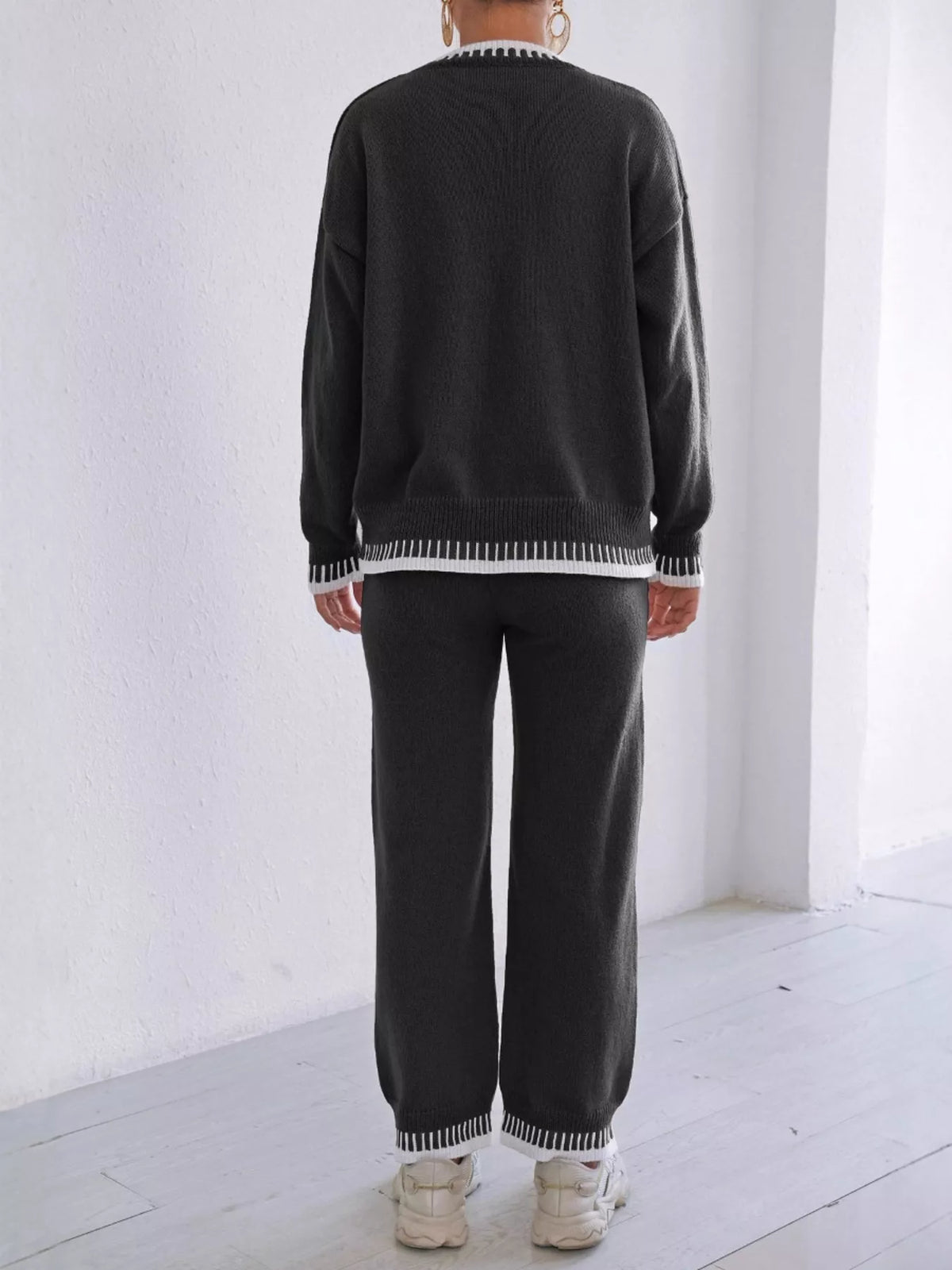 Back view of the black sweater and pants set with white contrast edging at the hems.