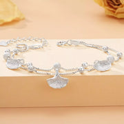 Double-layer silver ginkgo bracelet laid flat on a warm-toned display