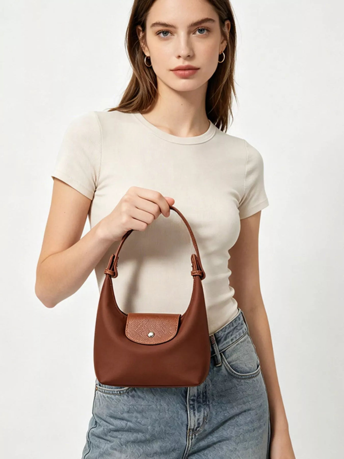 Model holding the short handle of the brown bag in front, showing its textured flap and metal snap.