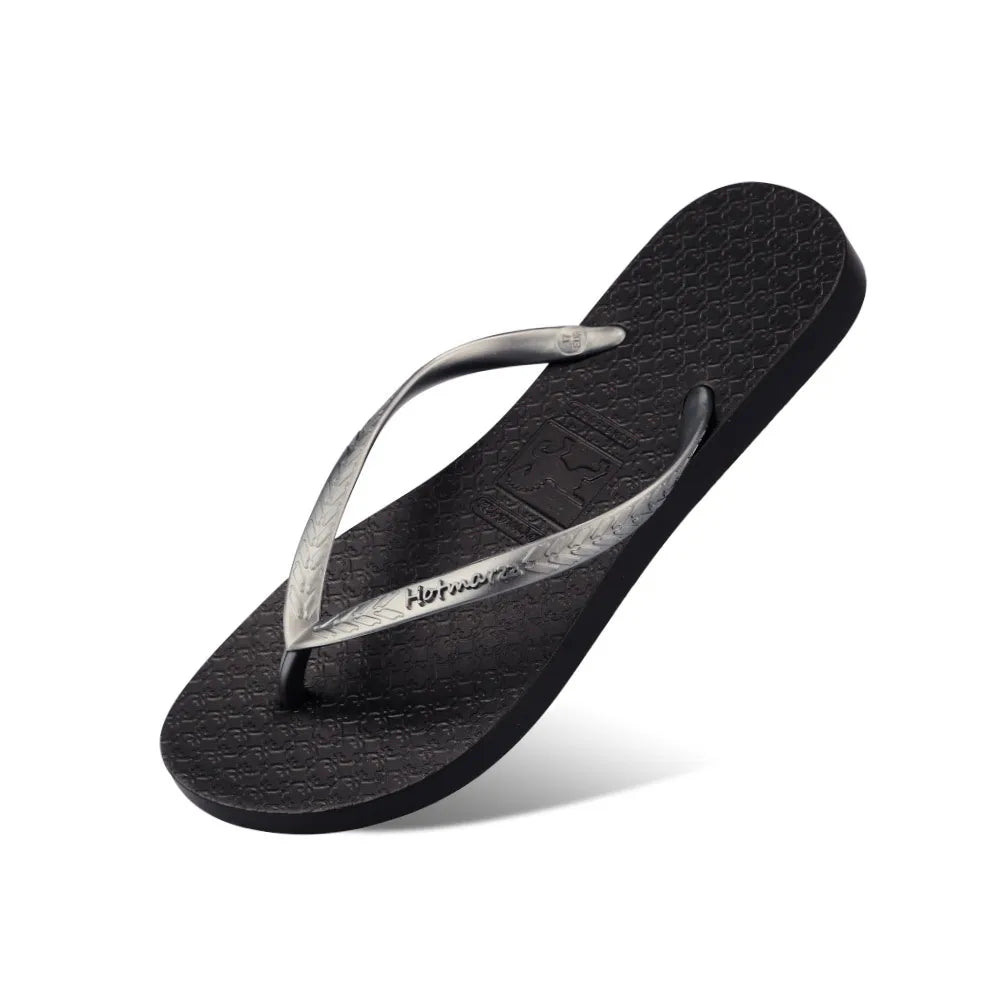 Black flat flip-flop with silver-coloured straps, angled view on white