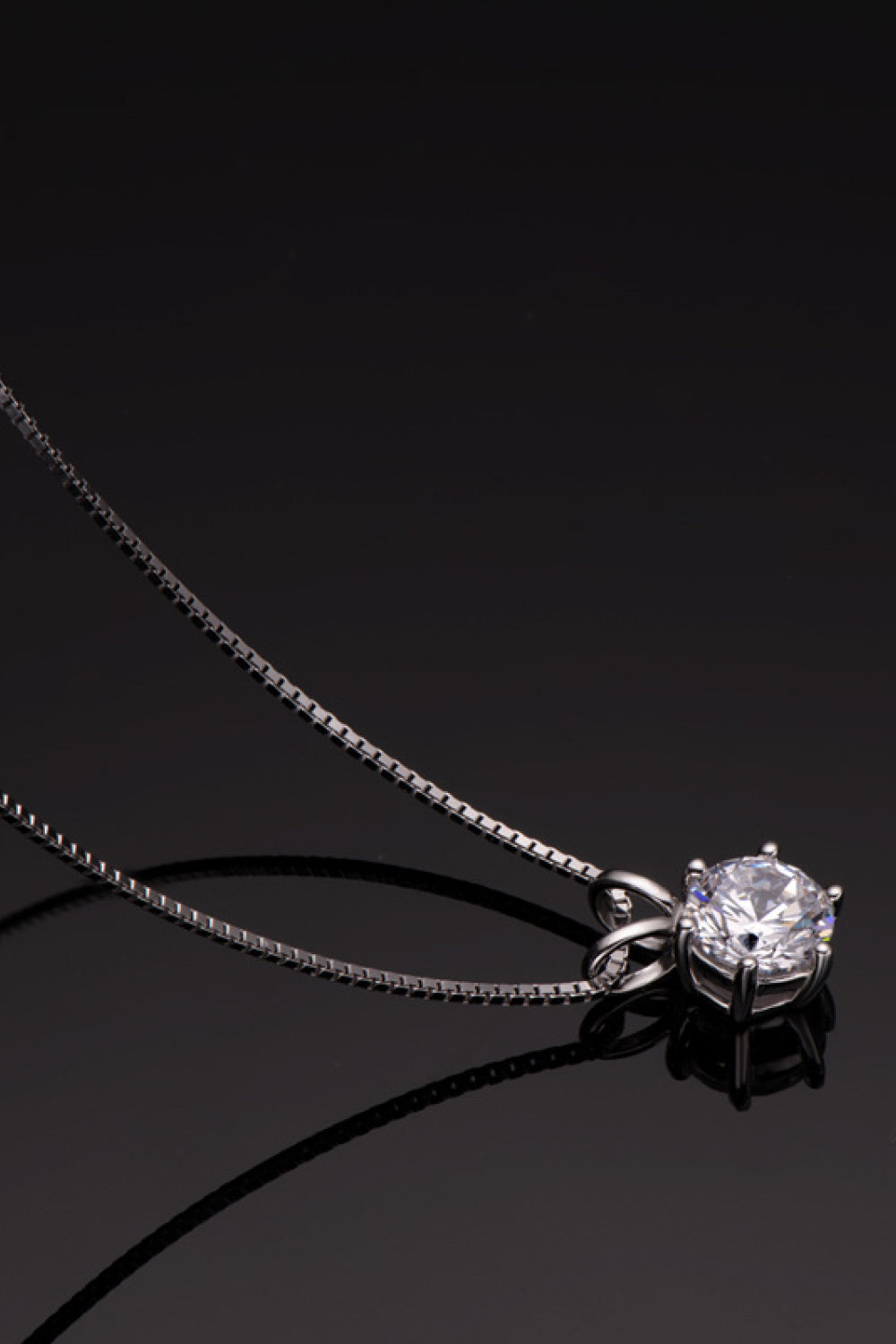 Silver-tone solitaire pendant necklace reflected on a glossy black surface