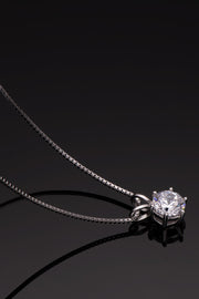 Silver-tone solitaire pendant necklace reflected on a glossy black surface