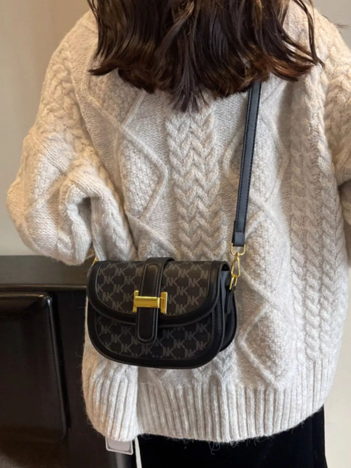Front view of black patterned shoulder bag with rounded flap and gold-coloured clasp