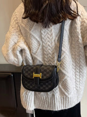 Front view of black patterned shoulder bag with rounded flap and gold-coloured clasp