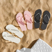 White, pink and black toe-post flip-flops arranged on sand