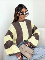 Seated model wearing cream and brown oversized sweater with broad vertical stripes