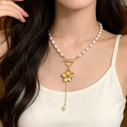 Close-up of pearl choker necklace with gold flower pendant and dangling pearl
