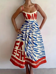 Model wearing a white spaghetti-strap midi dress with red lettering and blue sardine motifs, hands on hips.