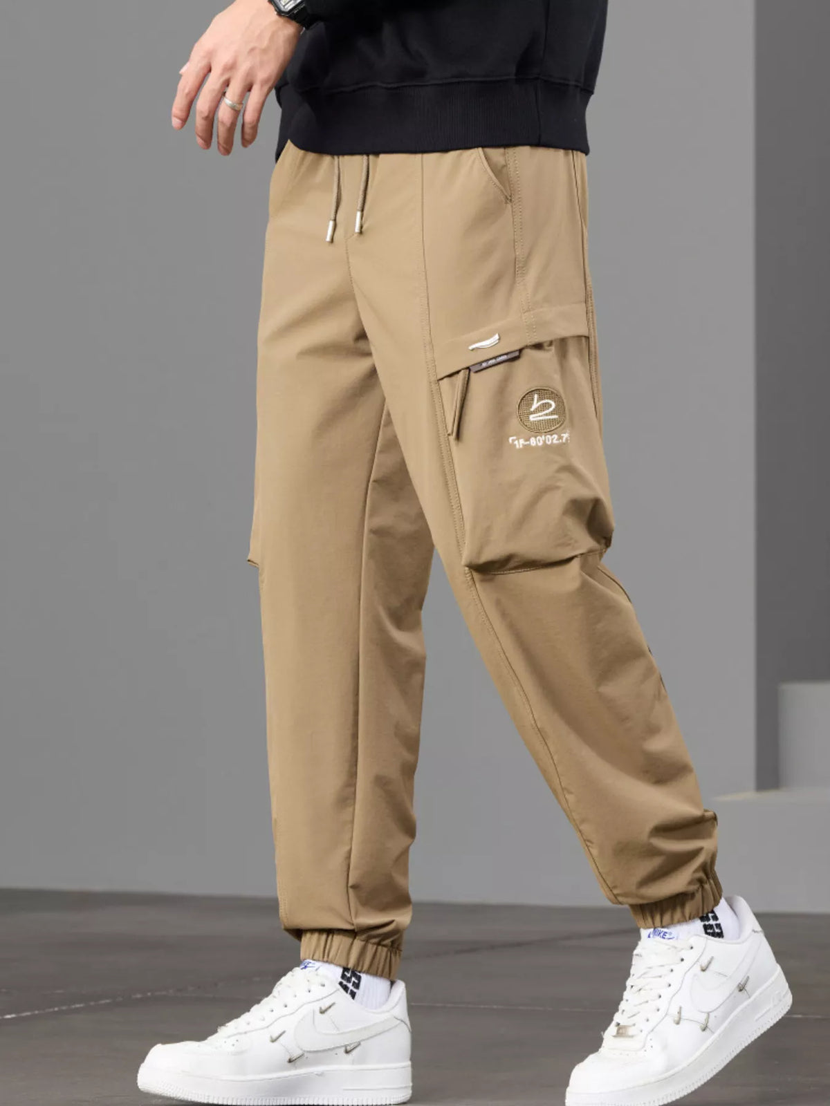 Angled front view of tan joggers showing the zip detail on the cargo pocket.