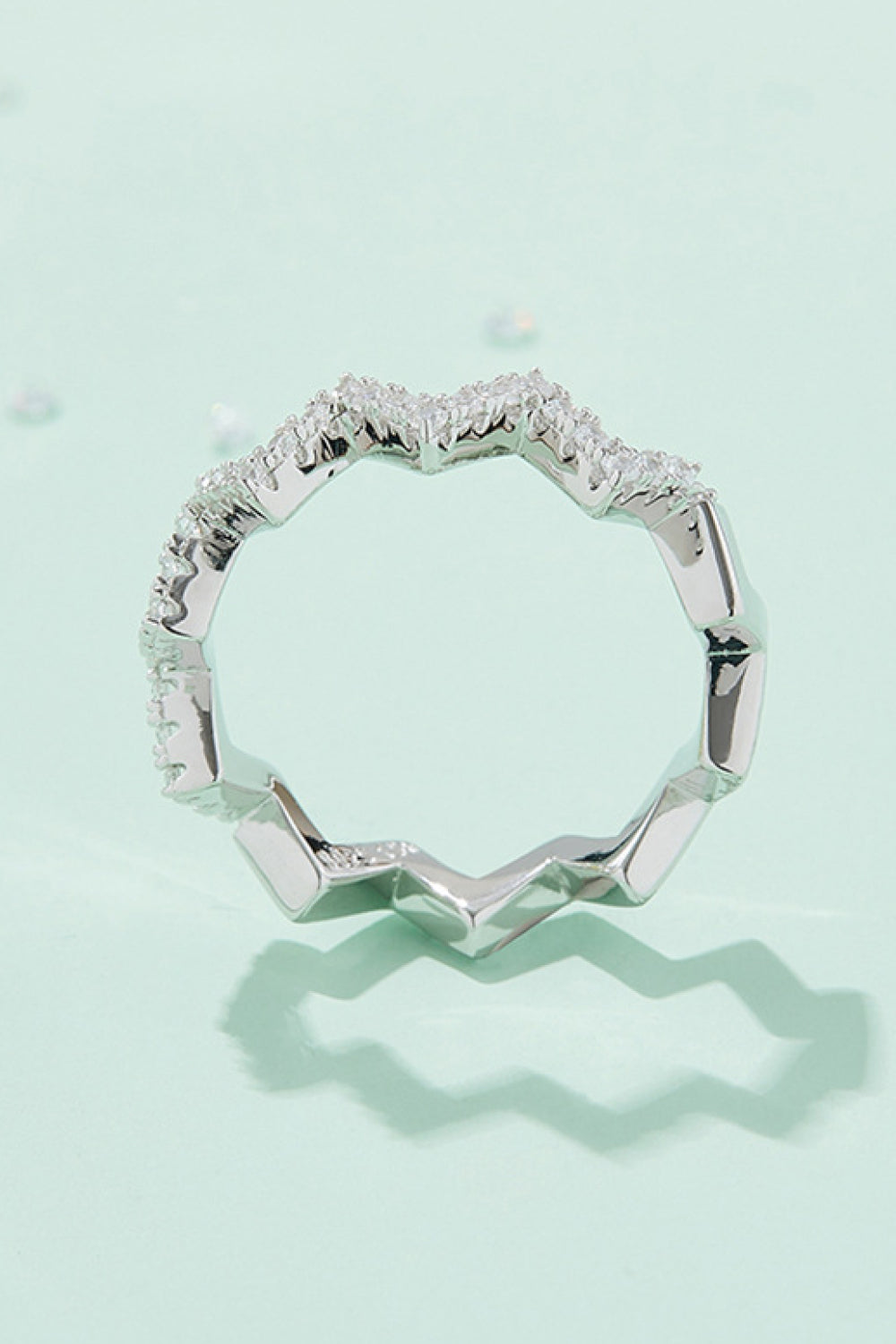 Top-down view of a platinum-tone moissanite ring with a wavy, stone-set band