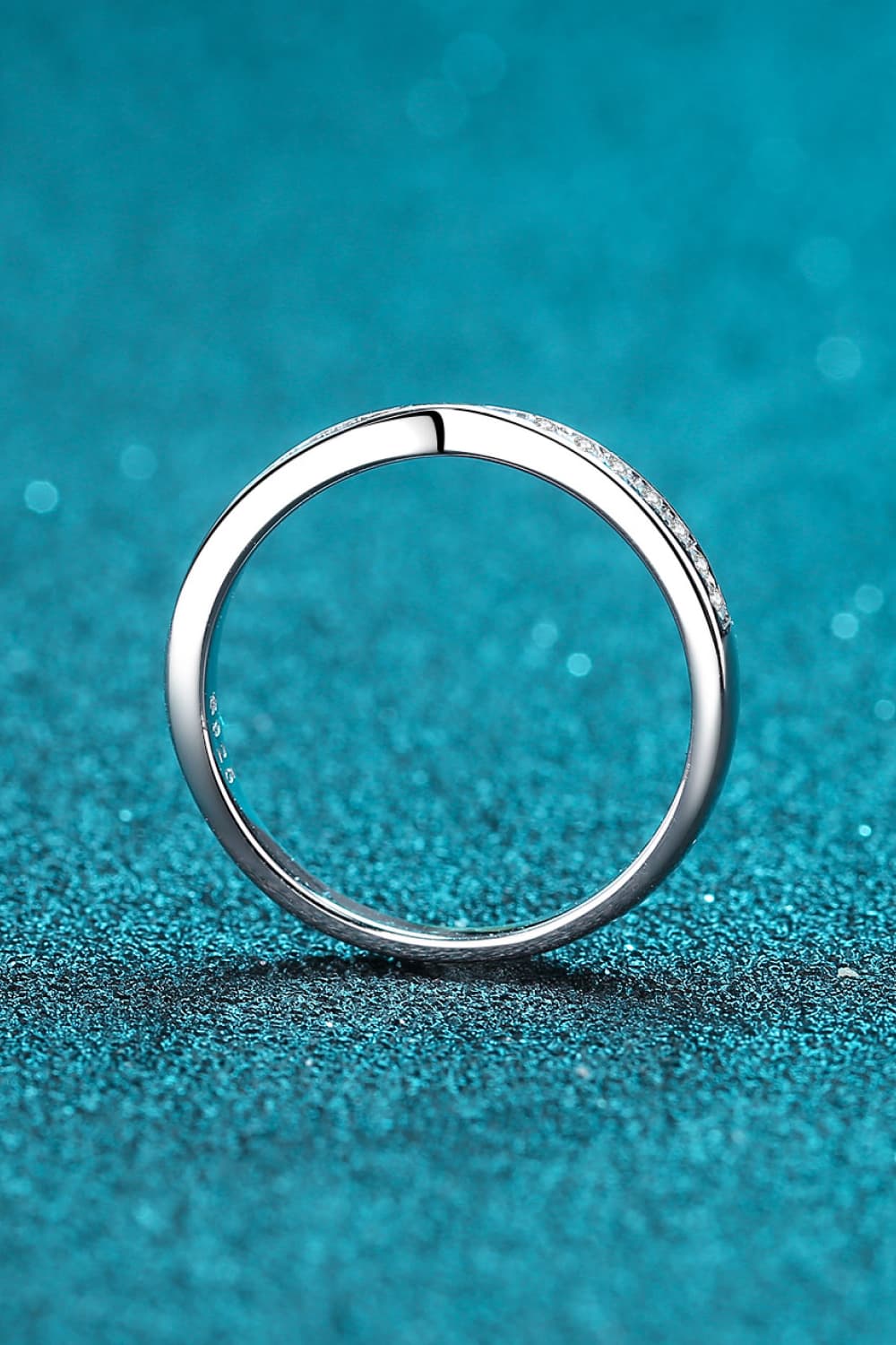 Back view of the plain circular band of a slim moissanite ring on teal.