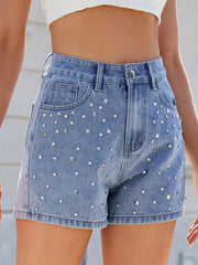 Blue studded denim shorts shown from an angle with front pockets and stitched hems
