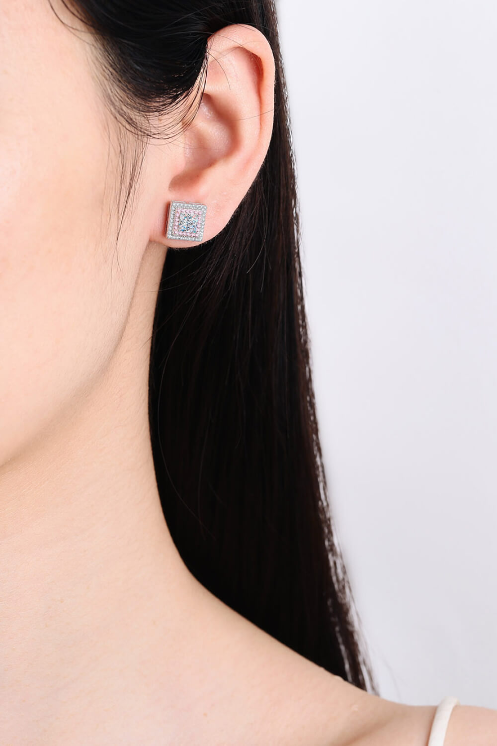 Square pink-and-clear stone stud earring worn on an ear