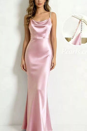 Model wearing a blush pink satin maxi dress with pearl straps and a draped cowl neckline.