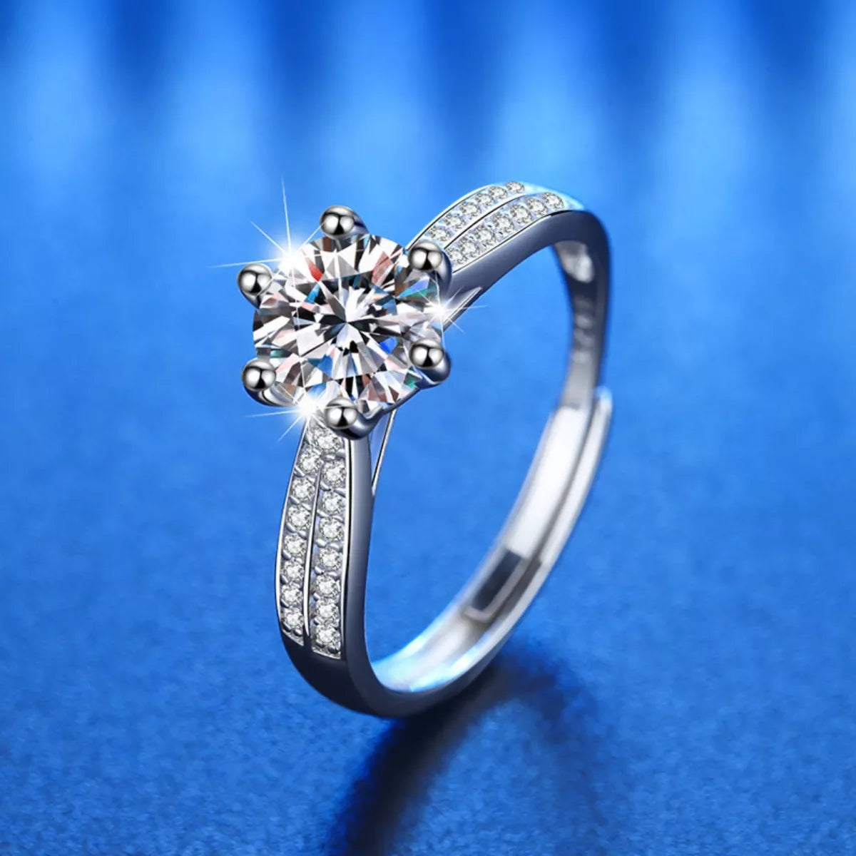 Angled view of a silver moissanite ring with a round center stone and pavé-set split band on blue