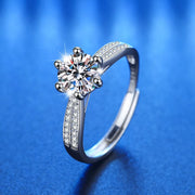 Angled view of a silver moissanite ring with a round center stone and pavé-set split band on blue