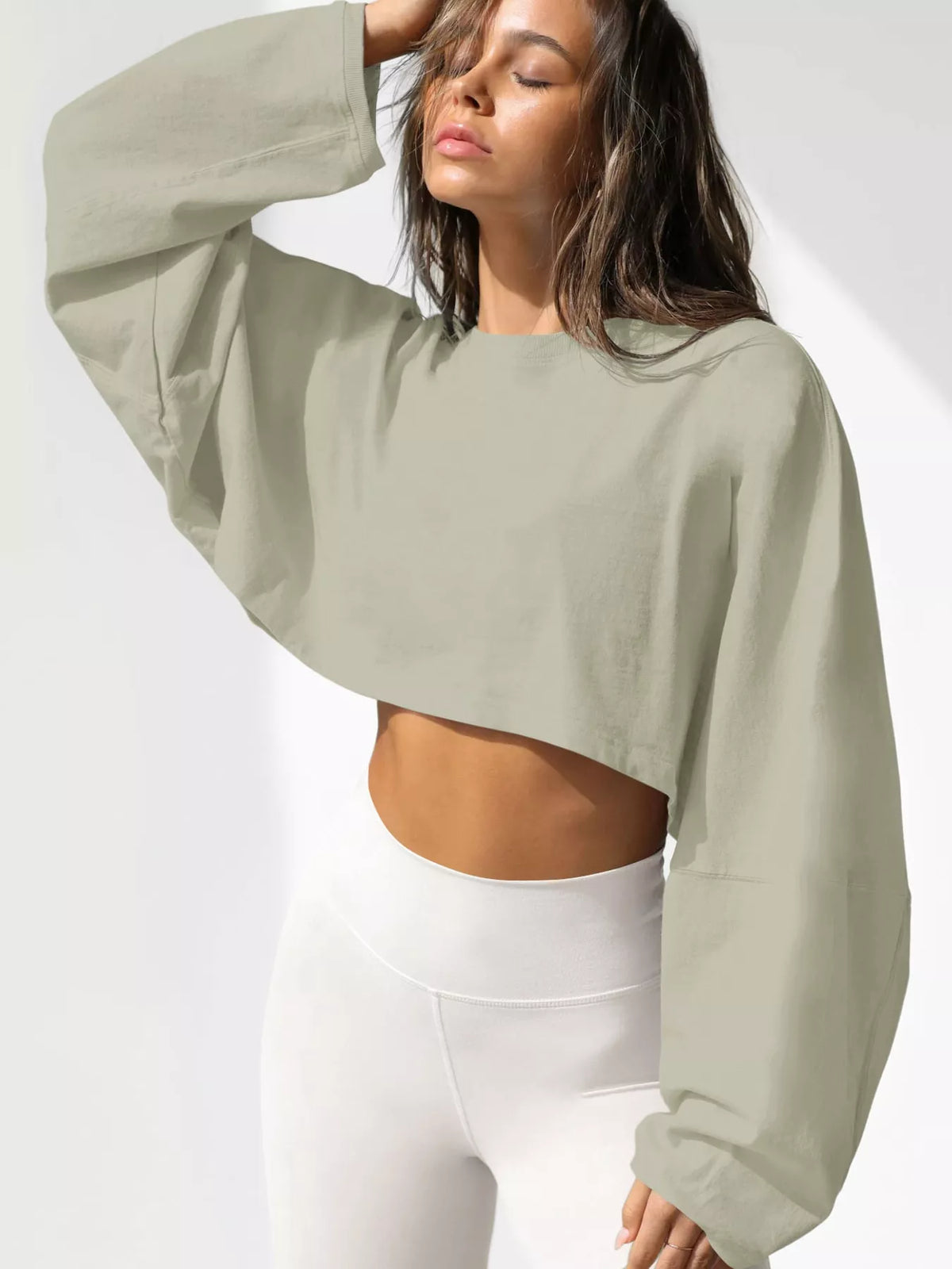 Front view of a pale sage cropped sweatshirt with oversized sleeves, worn with white leggings.