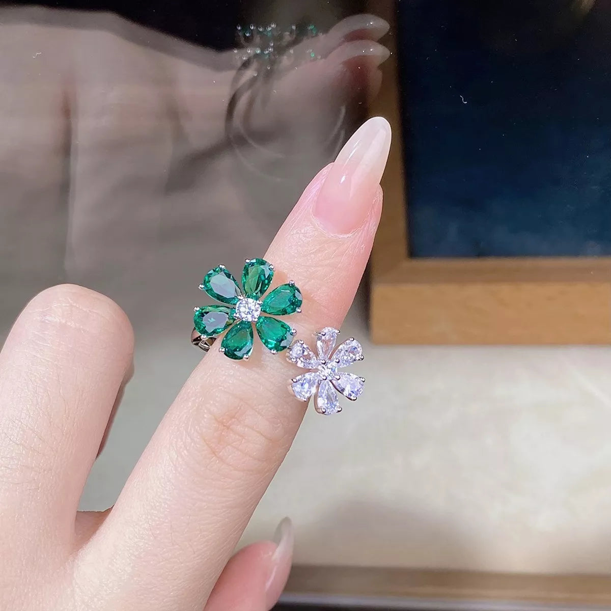 Green and clear flower-shaped ring worn on a hand, viewed from above