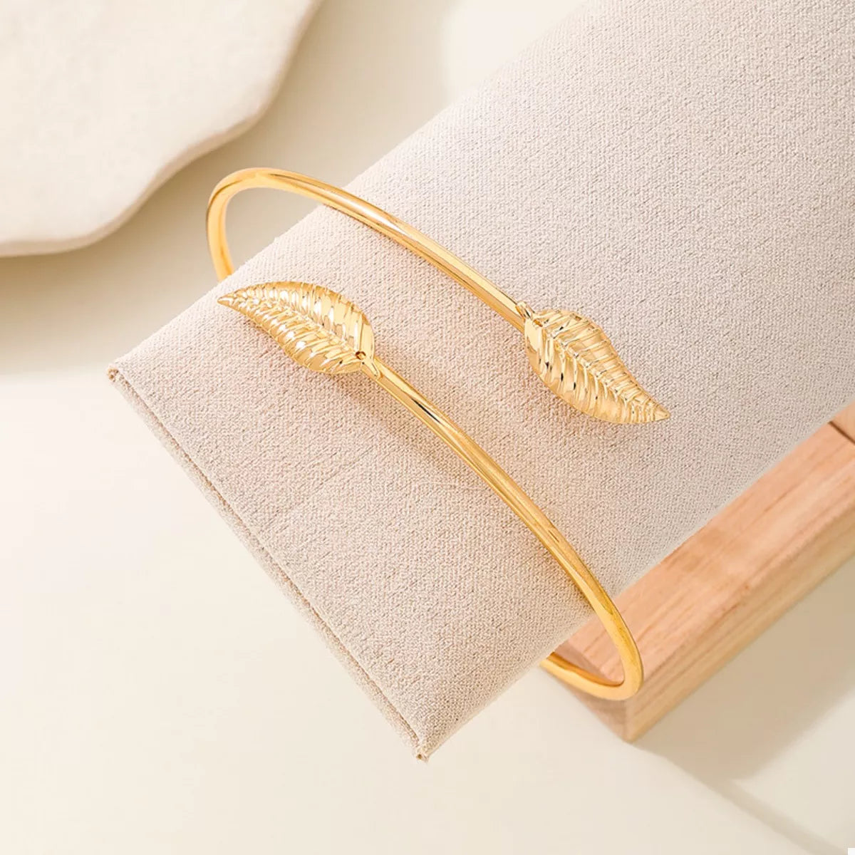 Gold-tone cuff bracelet with textured leaf ornaments on display block