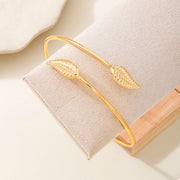 Gold-tone cuff bracelet with textured leaf ornaments on display block