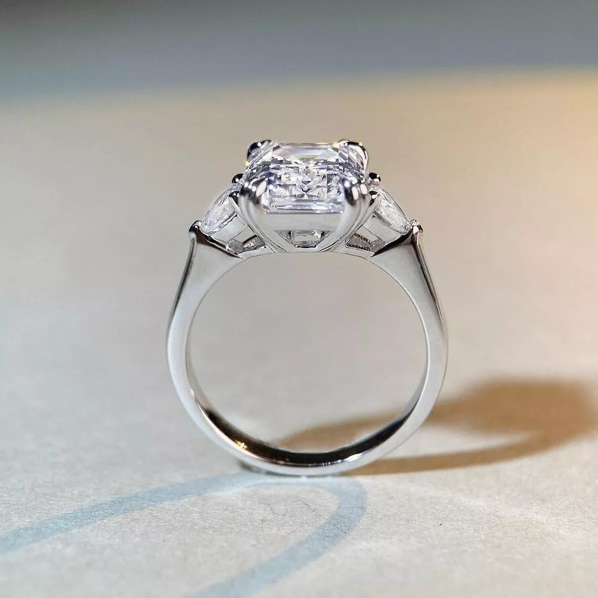 White-metal ring with a large clear emerald-cut center stone, viewed from the side to show the setting