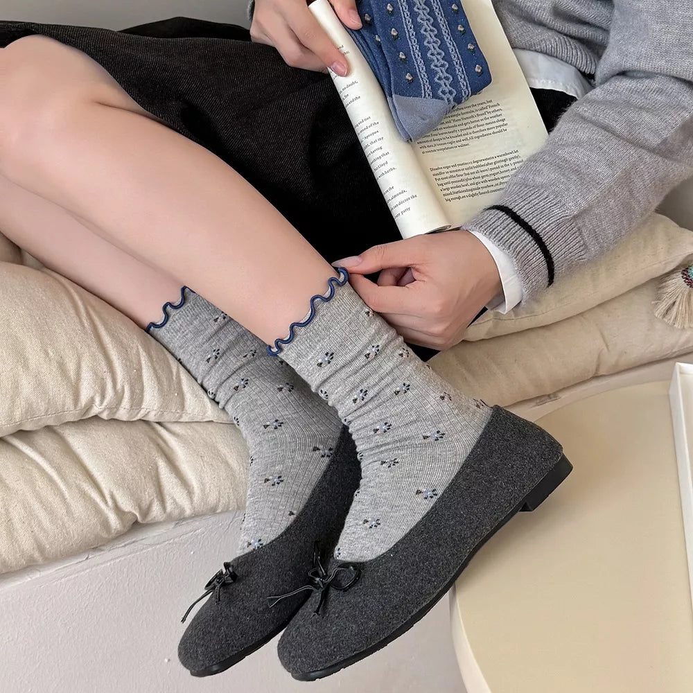 Pair of gray socks with small dark motifs and navy scalloped cuffs, worn with loafers